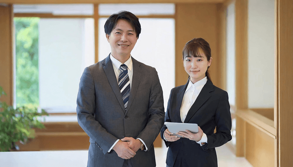 スーツ姿の男女2人が笑顔で並ぶビジネスポートレート、女性はタブレットを持っている
