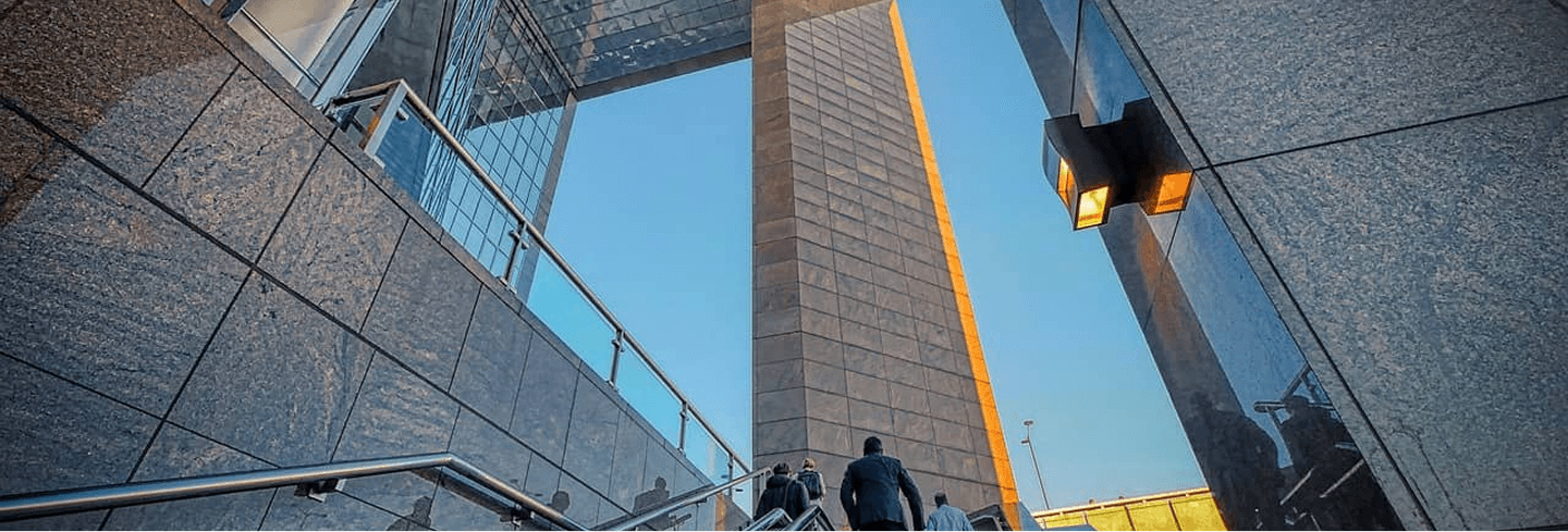 近代的な高層ビルの間を階段で上るビジネスマンたち、青空を背景にした都市の風景