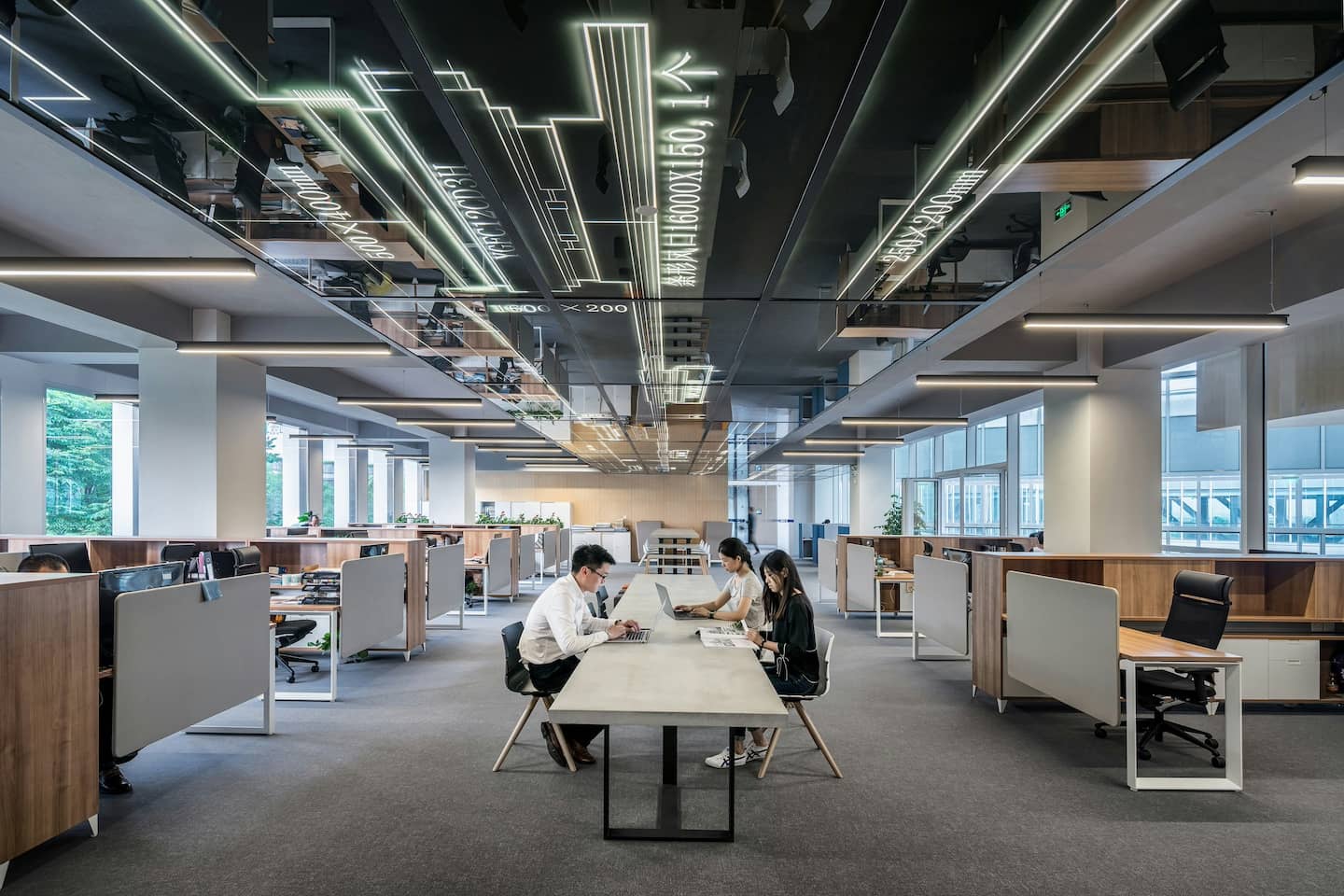 モダンで開放的なオフィス空間、中央の共有テーブルで作業する社員たちと周囲のデスクブース